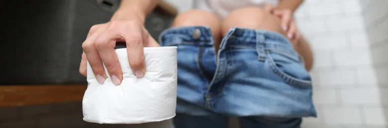 Osoba sedící na záchodě s toaletním papírem v ruce.
