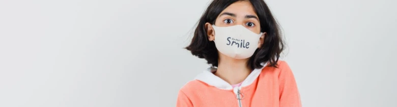 Dívka v roušce s nápisem Smile na bílém pozadí.