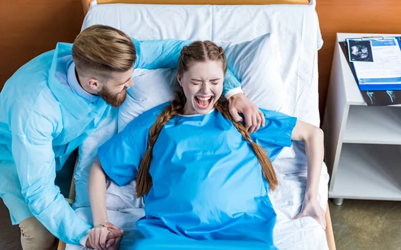 Žena v porodním sále zažívá bolestivé kontrakce při porodu.