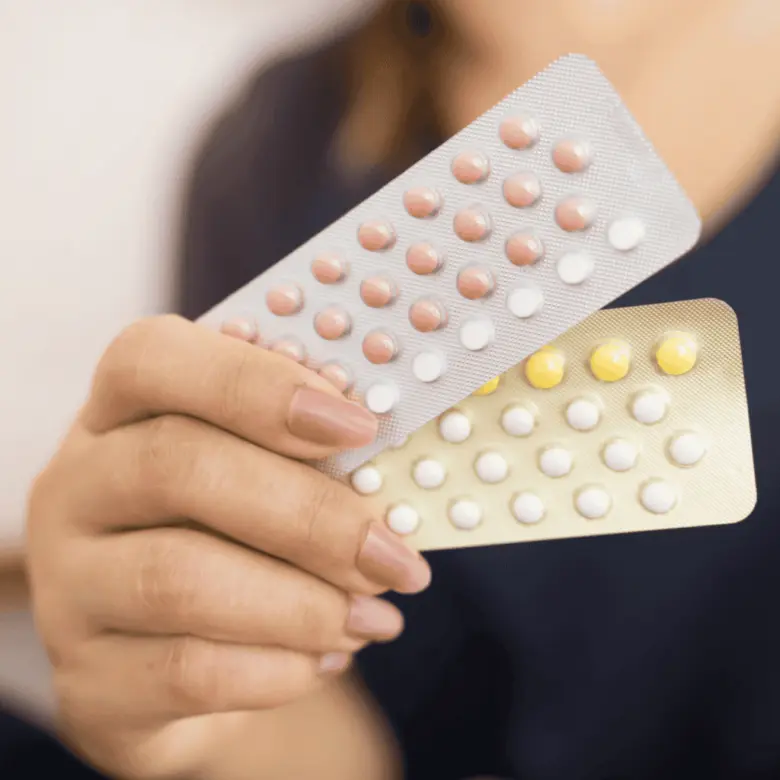 Ruka drží balení hormonální antikoncepce s různobarevnými pilulkami.