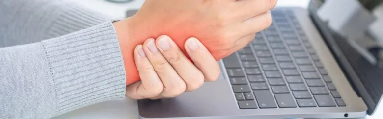 Člověk drží bolavý zápěstí u klávesnice při syndromu karpálního tunelu.