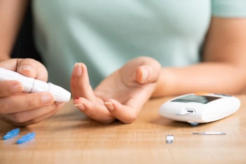 Měření hladiny cukru v krvi pomocí glukometru na dřevěném stole.