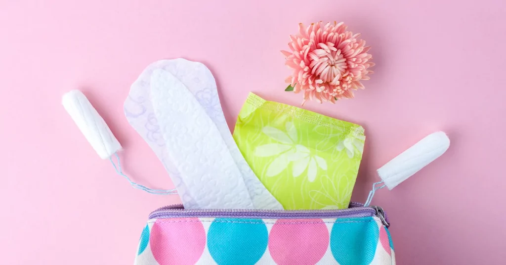 Koloritní taška s menstruačními výrobky na růžovém pozadí.