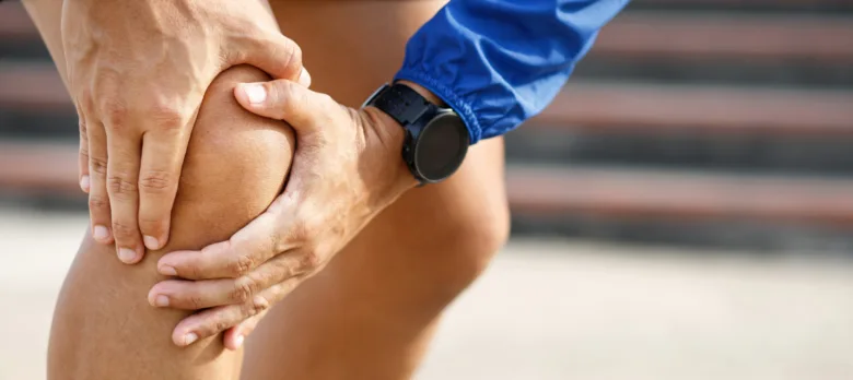 Muž drží bolestivé koleno rukama po sportovním tréninku.