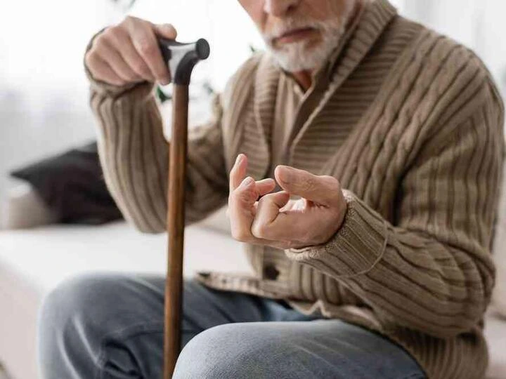 Starší muž s holí ukazuje třes ruky při Parkinsonově chorobě.