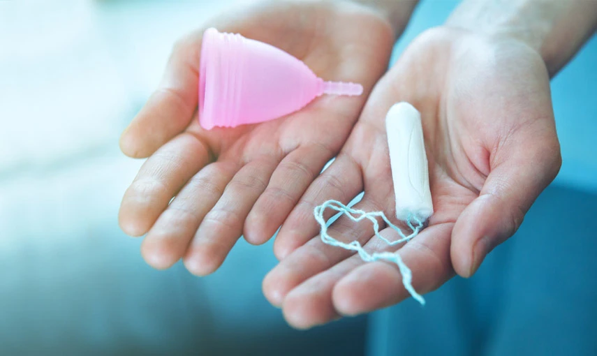 Ruce drží růžový menstruační šál a bílý tampón.