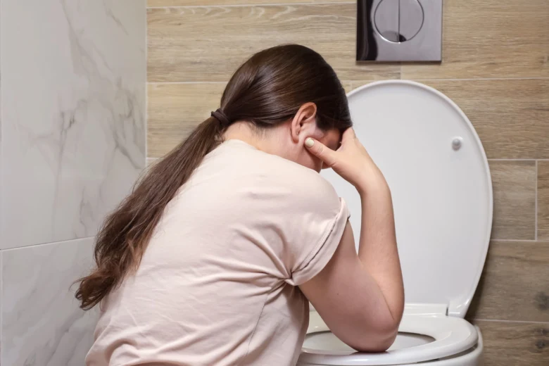 Žena sedí na záchodě s bolestmi v břiše.