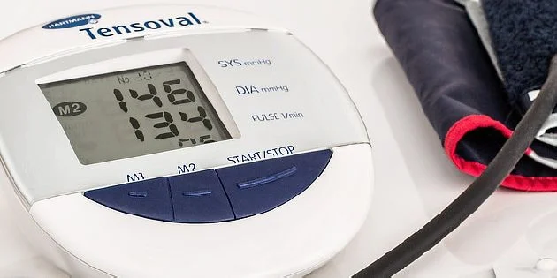 Digitální měřič krevního tlaku s manžetou na bílém povrchu.