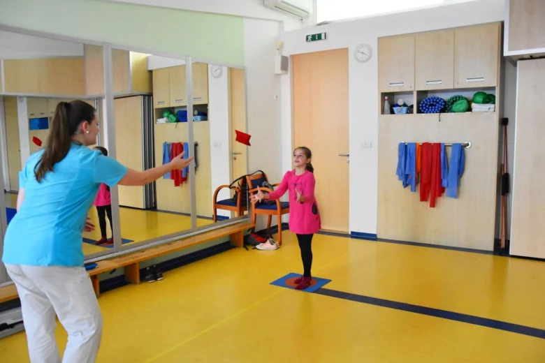 Terapeutka pomáhá dítěti cvičit v rehabilitační místnosti.