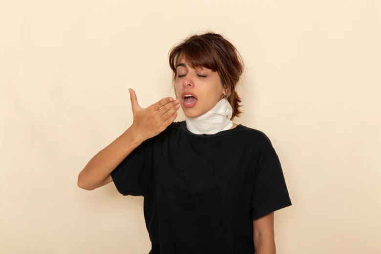Žena s krční ortézou kašle nebo yká, příznak bolesti v krku.