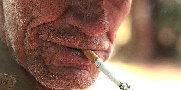 Starší muž kouří cigaretu s vykašláváním.