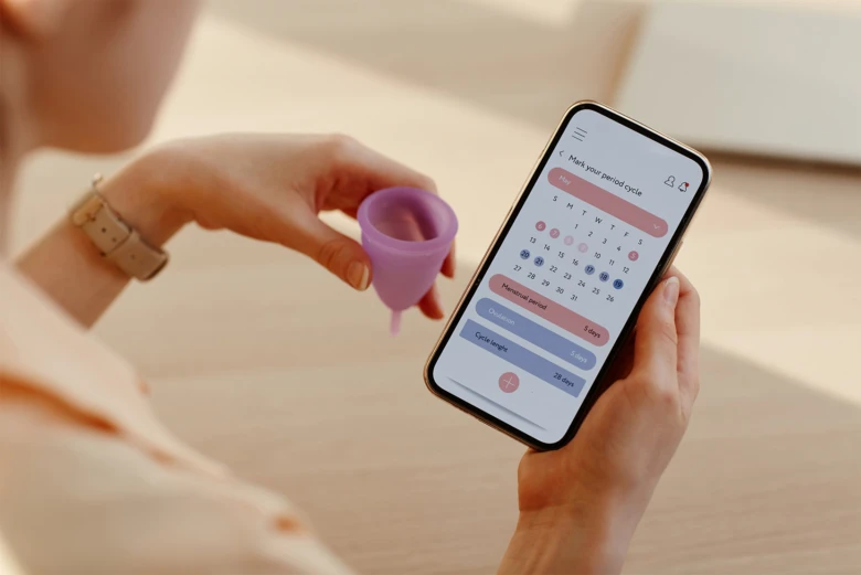 Žena drží menstruační šálku a používá aplikaci pro sledování cyklu.