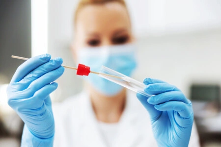 Laborantka drží vzorkovací štětec ve zkumavce