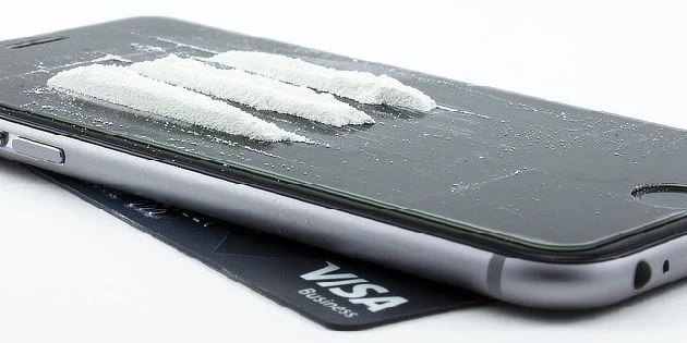 Bílý prášek kokainu na displeji mobilního telefonu.