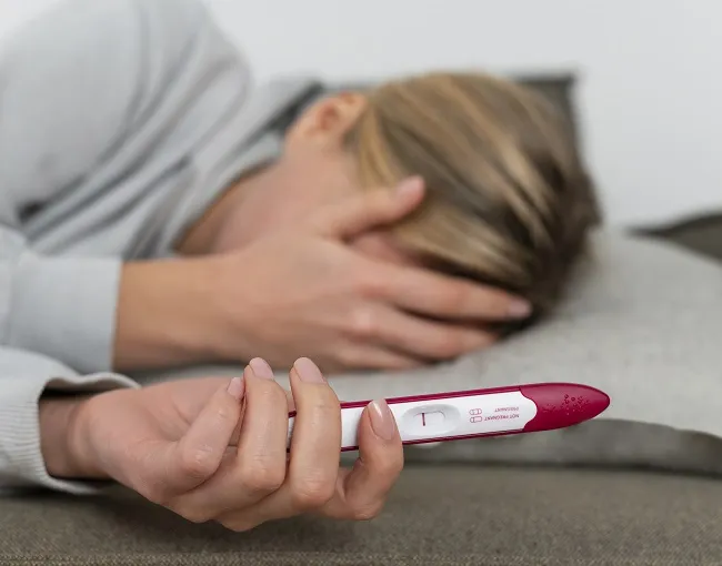 Žena drží těhotenský test s pozitivním výsledkem.
