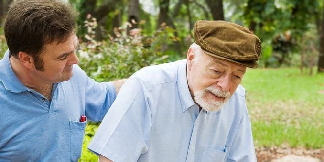 Mladý člověk pomáhá starému muži v přírodě.