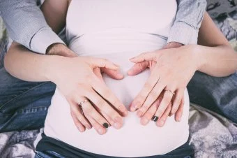 Ruce na břichu těhotné ženy v bílé podvazu.