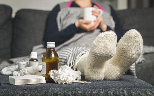 Osoba v šátku s léky na gauči při bolesti břicha.