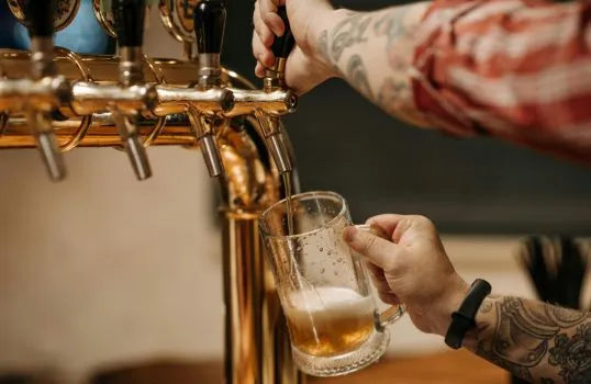 Člověk nalévá pivo z kohoutku do sklenice.