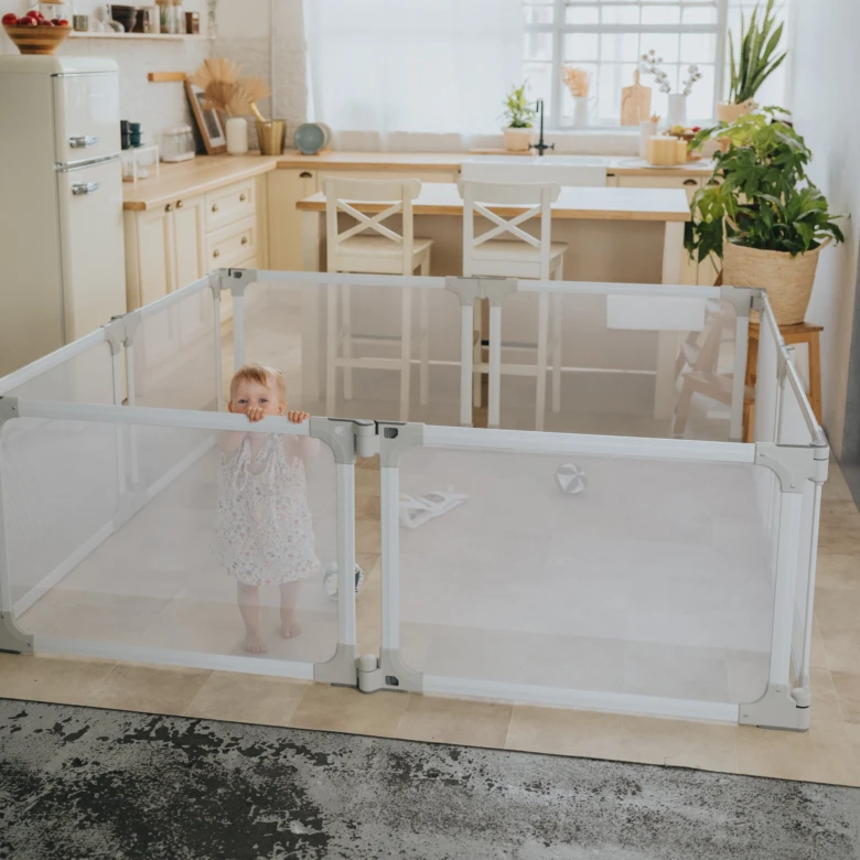 Béba v bílém hrací bariéře s mřížovými panely.