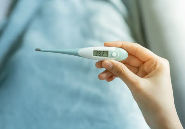 Digitální teploměr v ruce ukazuje zvýšenou tělesnou teplotu.