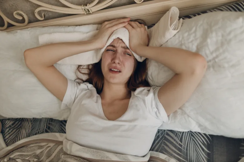 Žena leží v posteli s hlavou ve dlaních při migréně.