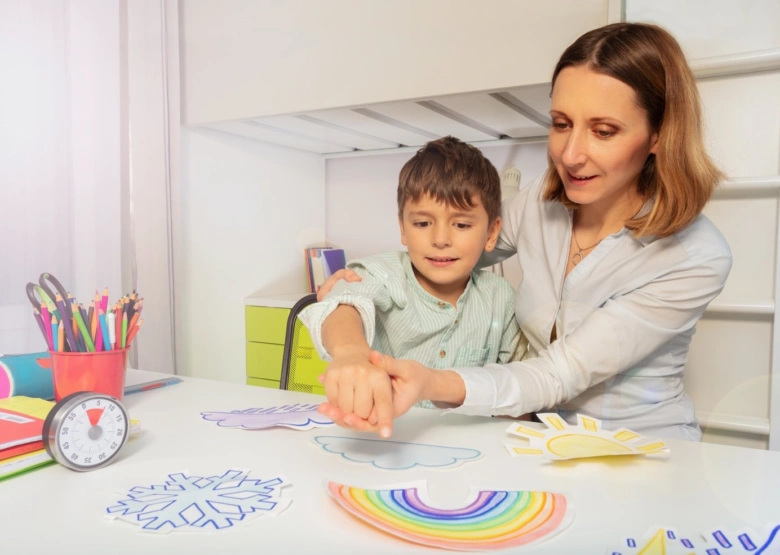 Žena pomáhá chlapci kreslit barevné tvary na papíru.