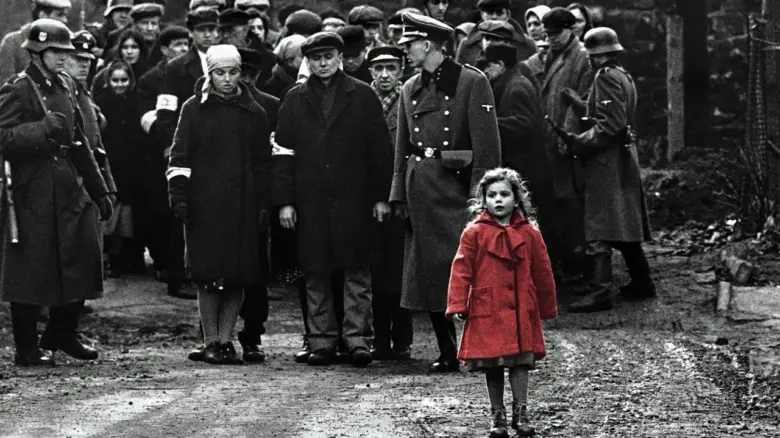 Dívka v červeném kabátě stojí před vojáky a civilisty na historické scéně.