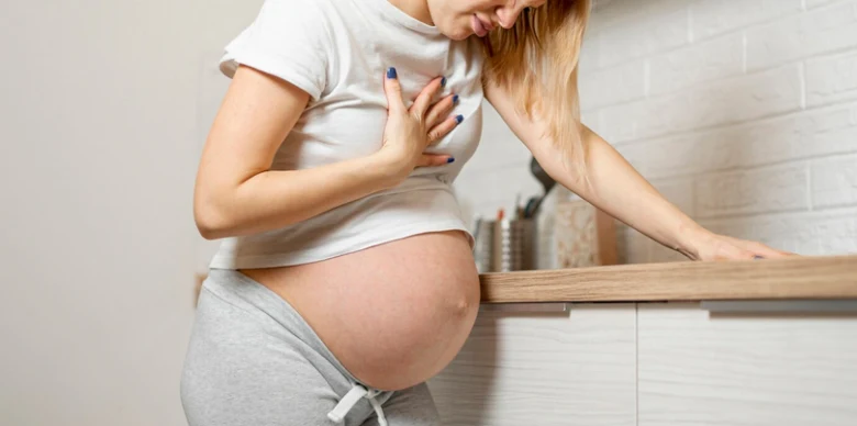 Těhotná žena drží ruku na svém břiše v kuchyni.