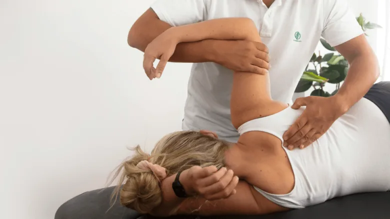 Fyzioterapeut provádí manuální terapii ramene pacientce ležící na stole.