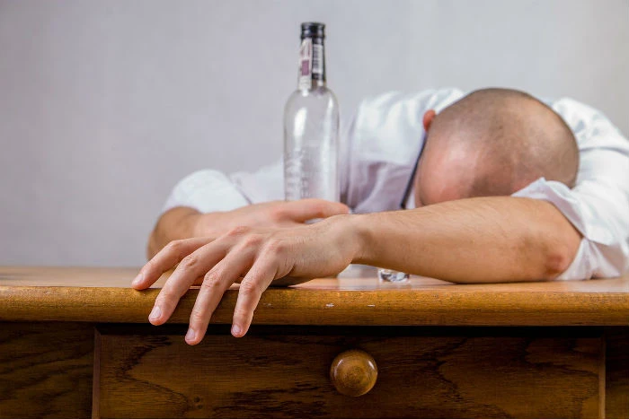 Muž leží na stole vedle lahvě alkoholu jako příznak zneužívání.