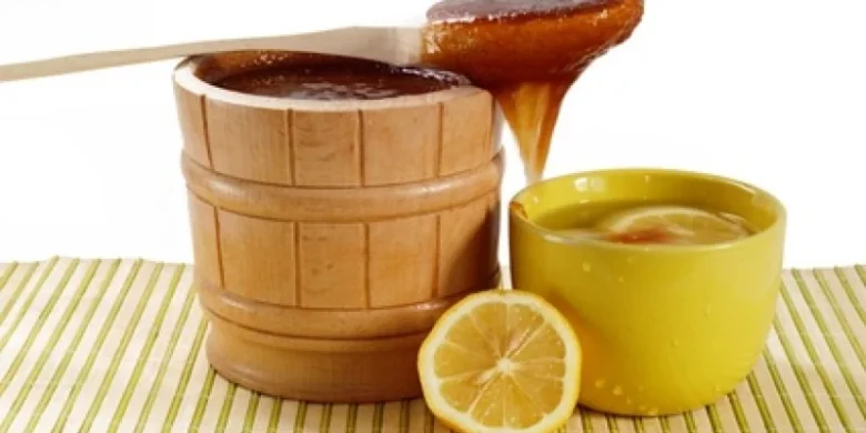 Dřevěná nádoba s medem, citronová polovina a žlutá miska.