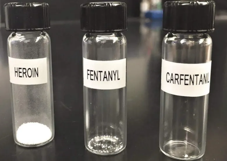 Tři skleněné nálevky s bílými prášky označené heroinem, fentanylem a karfentanilem.
