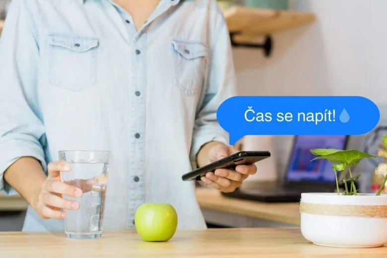 Muž pije vodu z skla s mobilním telefonem na stole.