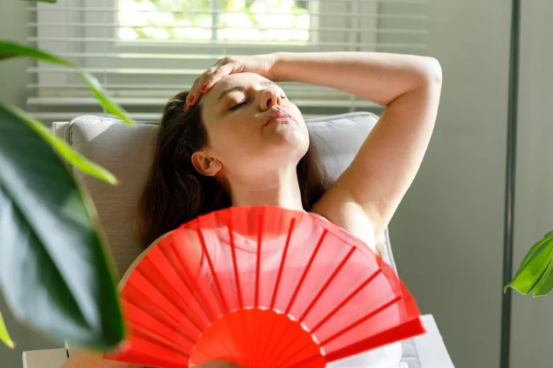 Žena se chladí červeným ventilátorem při příznacích úžehu.