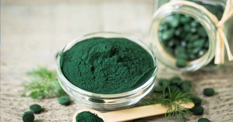 Skleněná miska s práškem z řasy Spirulina vedle tablet.