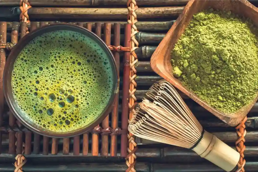 Připravený čaj matcha s práškem v dřevěné mísce na bambusové podložce.