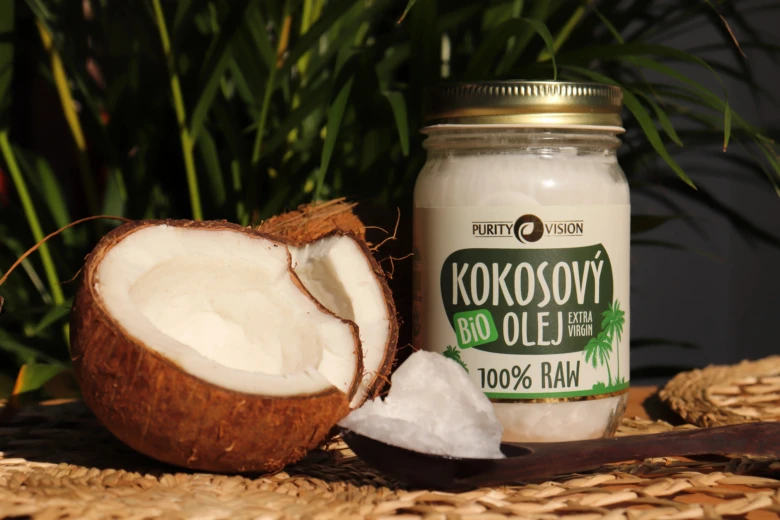 Sklenice s kokosovým olejem vedle rozkrojeného čerstvého kokosu.
