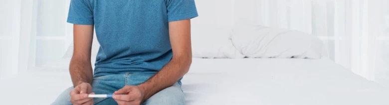Muž sedící na posteli drží v rukou diagnostický proužek.