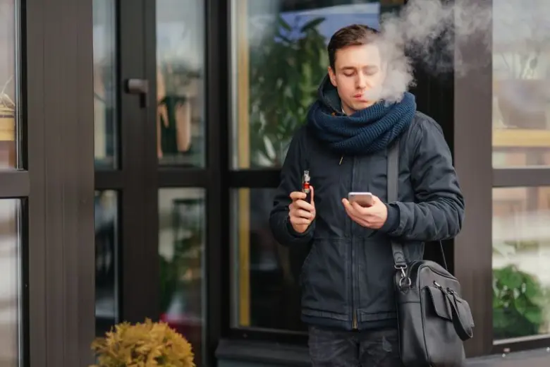 Muž v zimě vapuje venku s elektronickou cigaretou.
