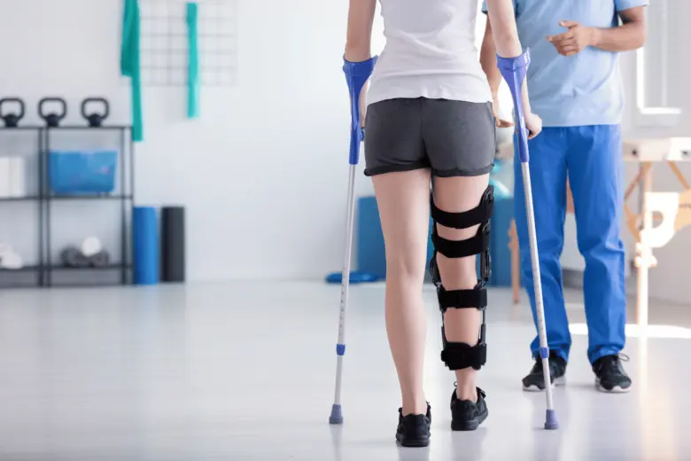 Pacient s holí a ortézou na koleno při rehabilitaci.