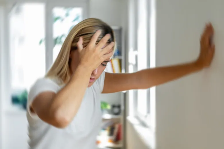 Žena s příznaky migrény drží hlavu u zdi.