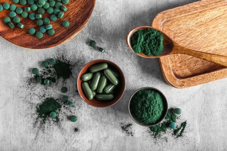 Spirulina v tabletách, kapsulích a prášku na dřevěných miskách.