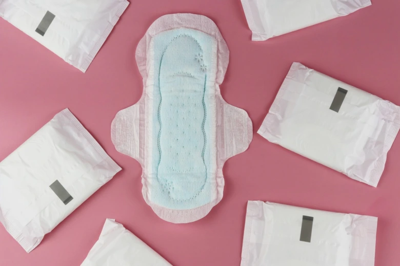 Menstruační vložka s obaly na růžovém pozadí.