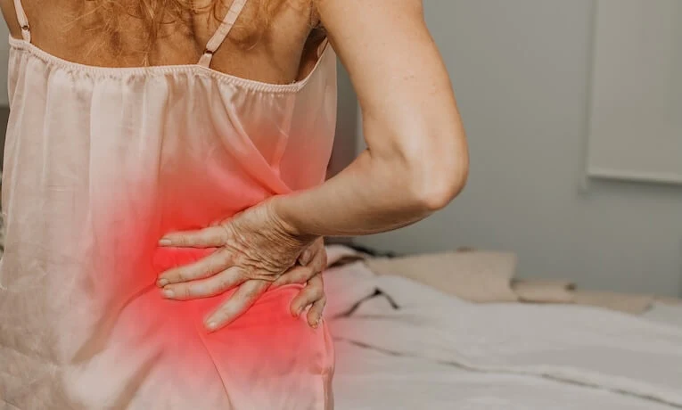 Žena drží dolní část zad kvůli bolesti při skřípnutém nervu.