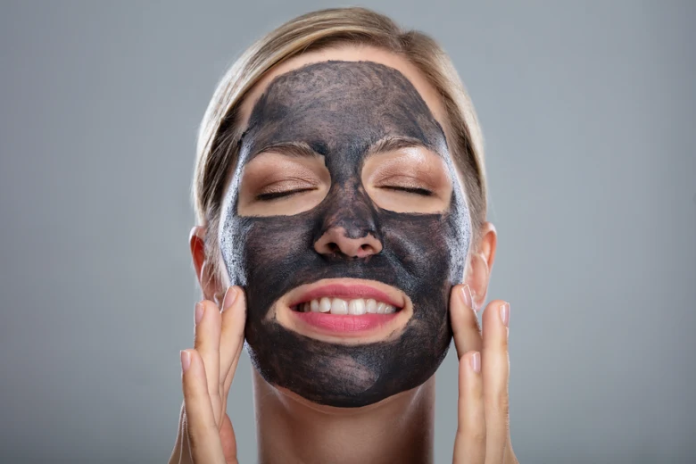 Žena aplikuje černou masku z aktivního uhlí na obličej.