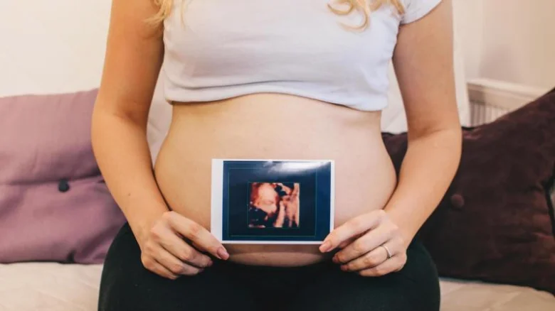 Těhotná žena drží ultrazvukový snímek na svém břiše.