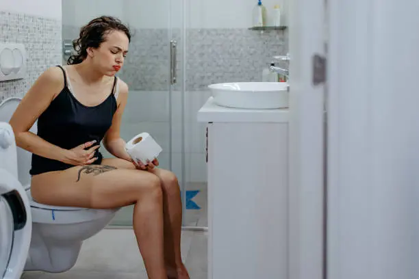 Žena sedí na záchodě s příznaky průjmu v koupelně.