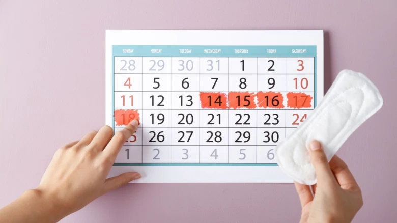 Ruce ukazují na kalendář s menstruačním tampónem.