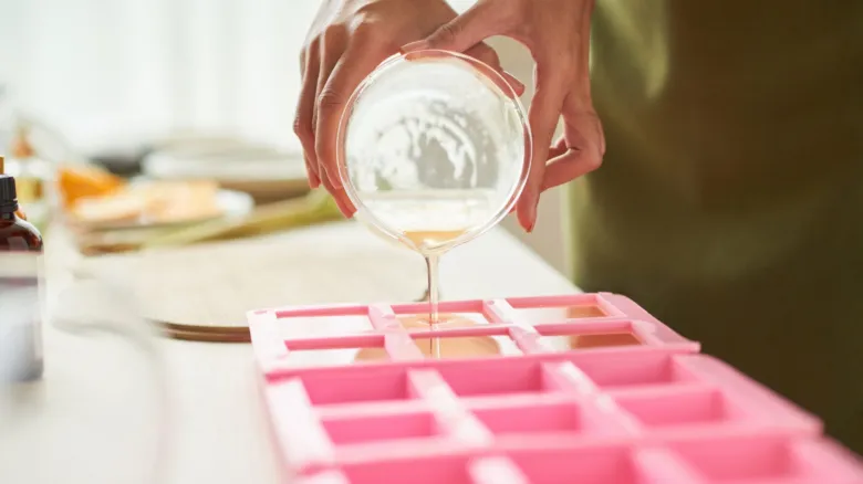 Ruce nalévají glycerol do silikonových forem na kuchyňském stole.